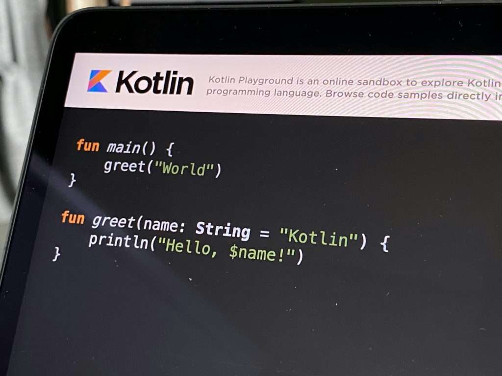 Ein Laptop-Bildschirm zeigt Kotlin-Code in einer Entwicklungsumgebung mit der Begrüßungsfunktion main() und der greet()-Funktion.